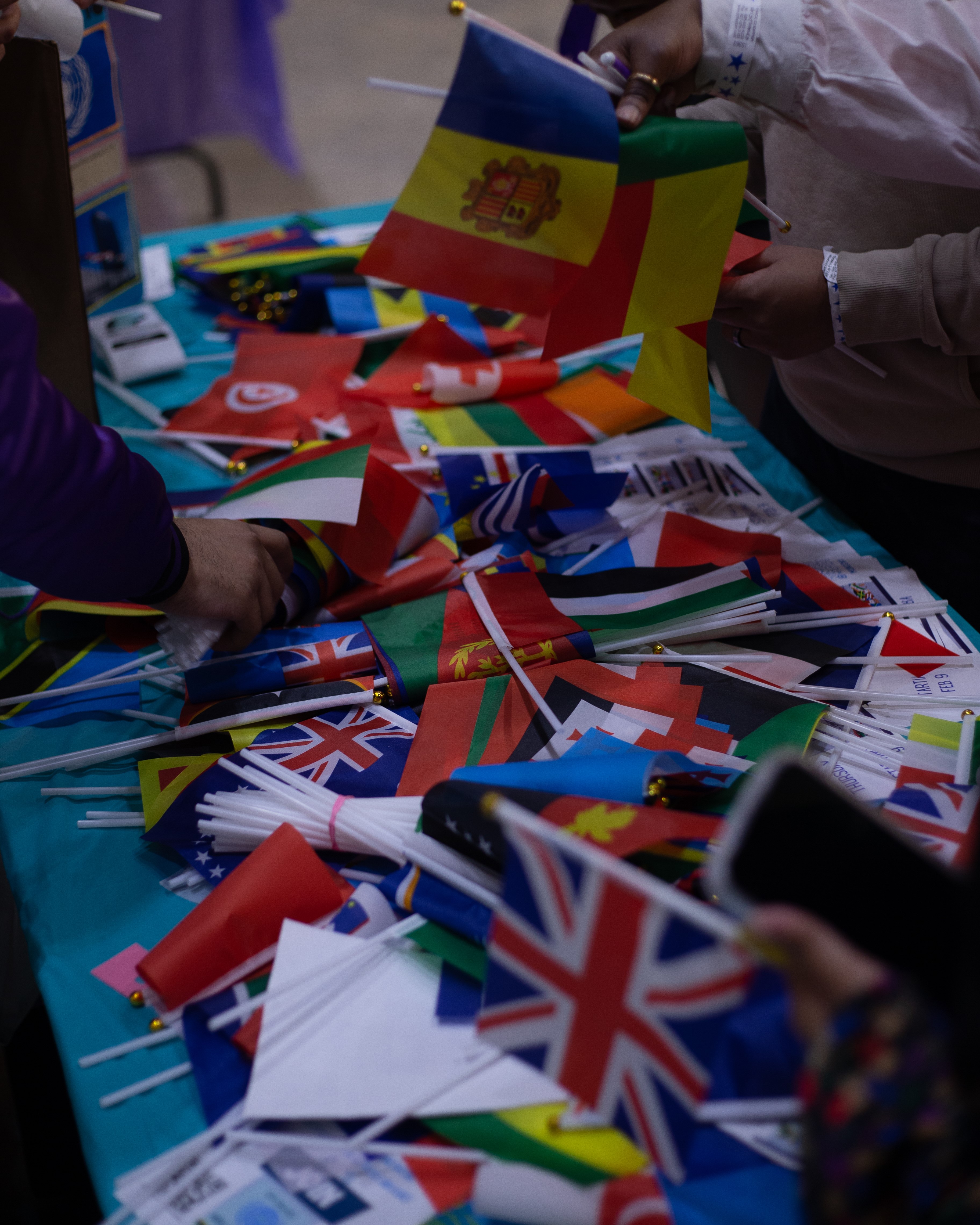 Individuals browsing and holding various international flags displayed on a table.