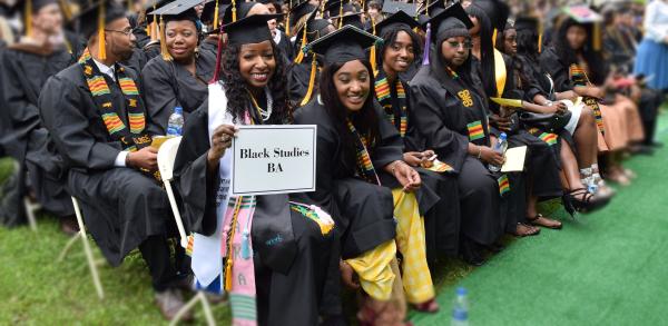 Students at the 2018 Graduation- they are all in cap and gown- about 30 people are int he photo but 5 are looking into the camera- they are holding a sign that reads " Black Studies BA" 