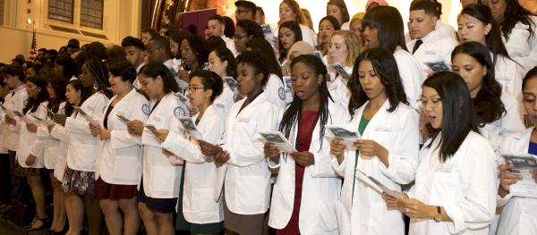 students wearing white coats at a ceremony in the great hall of shepard hall