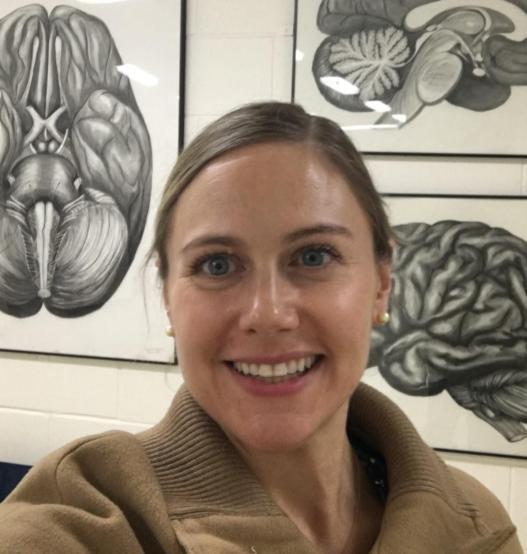 photograph of smiling professor in front of medical images of brains