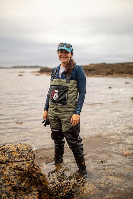 Photo of Melina Giakoumis standing in water with a cap and sun glasses on  head.